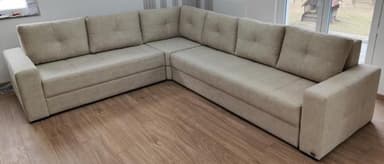An L-shaped modular sectional sofa upholstered in a light beige textured fabric, featuring tufted back cushions and wide, flat armrests. — 3D model