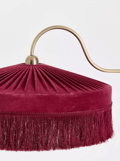A vintage-inspired arc floor lamp featuring a polished brass finish and a distinctive fringed velvet shade in burgundy. The lamp has a slender, straight stand rising from a circular base, transitioning into a gracefully curved arm that suspends the dome-shaped light shade. The shade is characterized by radial pleats on its upper surface and an elaborate fringe trim along its lower edge. — 3D model