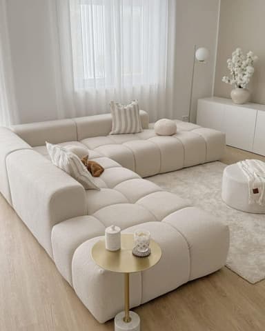A modular sectional sofa with a low profile and generous depth. The sofa features a tufted, pixelated design on its seat and back cushions, creating a contemporary aesthetic. It is upholstered in a textured, boucle-like fabric. Two throw pillows, one rectangular with striped pattern and one round, are placed on the sofa. The sofa is configured in an L-shape. — 3D model