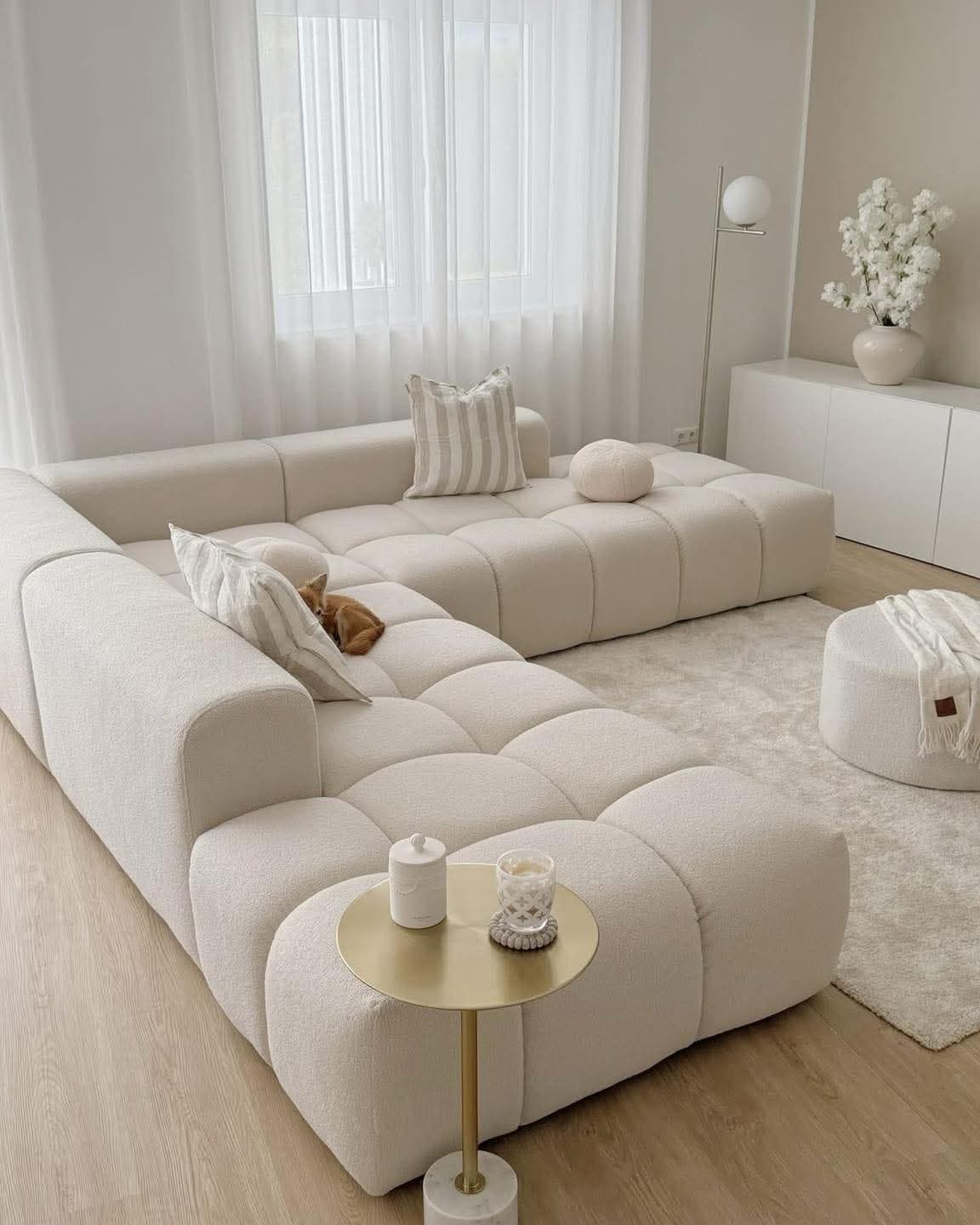 A modular sectional sofa with a low profile and generous depth. The sofa features a tufted, pixelated design on its seat and back cushions, creating a contemporary aesthetic. It is upholstered in a textured, boucle-like fabric. Two throw pillows, one rectangular with striped pattern and one round, are placed on the sofa. The sofa is configured in an L-shape. — 3D model