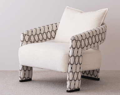 A contemporary upholstered armchair featuring a plush, light-colored bouclé fabric on the seat and back, complemented by patterned armrests and legs with a geometric design in black, white, and a coppery tone. It includes a matching back cushion. — 3D model