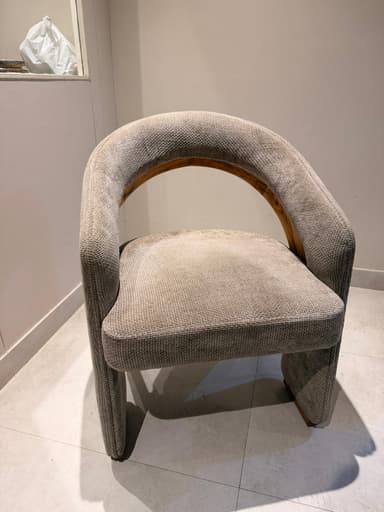 A contemporary armchair with a curved backrest and upholstered seat and arms. The frame appears to be constructed from wood, visible as a curved piece supporting the backrest. The upholstery is a textured fabric in a neutral tone. — 3D model