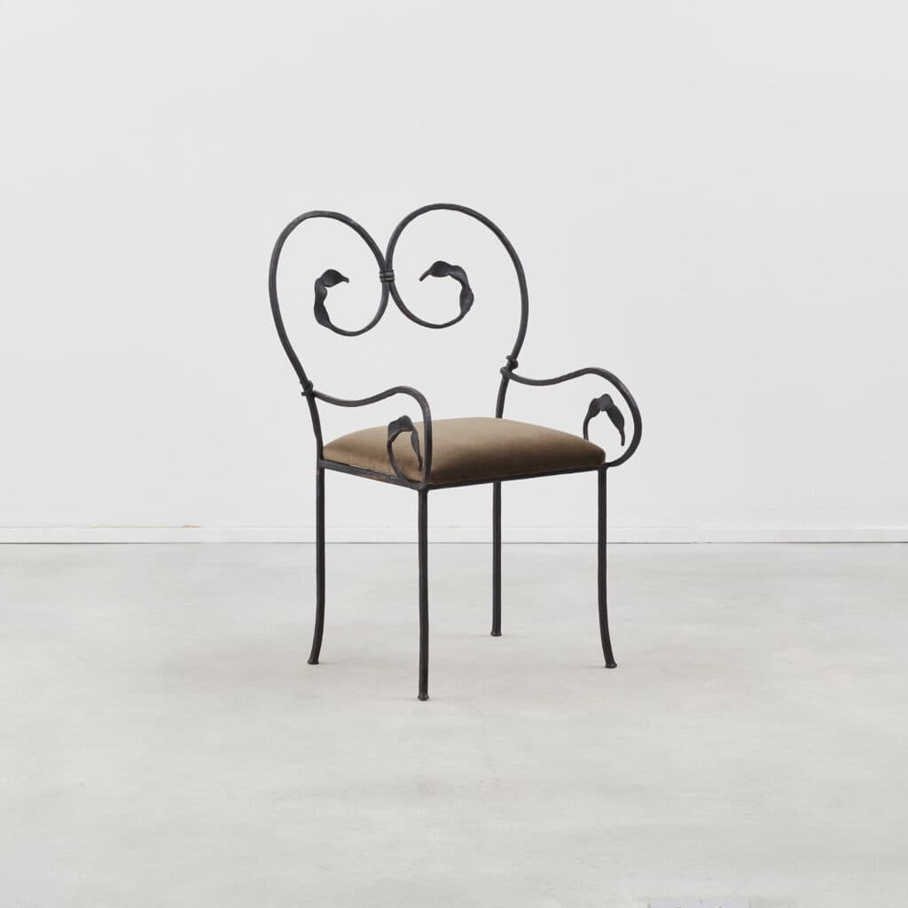 An ornate accent chair featuring a black wrought iron frame with scrolling details and a small, padded brown upholstered seat. The backrest forms a heart-like shape with stylized leaf motifs, echoed on the integrated armrests. The legs are slender and slightly curved, with small feet. — 3D model