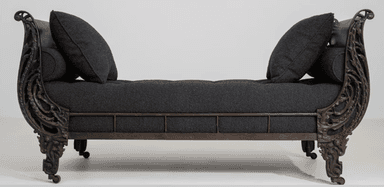 An ornate traditional recamier daybed featuring a dark, possibly bronzed or antiqued metal frame with intricate scrolled and carved details on both raised ends and the legs. The main seating surface is a deep button-tufted cushion upholstered in a dark gray or charcoal fabric. It is accompanied by a matching square throw pillow and a cylindrical bolster pillow. — 3D model