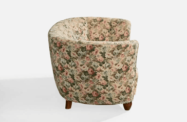 A vintage-style, curved sofa upholstered in a floral fabric with a pastel color palette. The sofa features a rounded backrest with vertical channeling and integrated armrests that curve inwards. It is supported by four short, tapered wooden legs. — 3D model