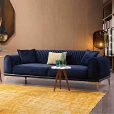 A contemporary three-seater sofa upholstered in deep navy blue velvet fabric, featuring channel tufting on the backrest and arms, supported by light wood legs with gold accents. — 3D model
