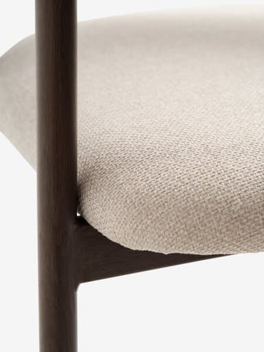 A contemporary dining chair featuring a dark brown wood frame and light beige fabric upholstery. The seat and backrest are padded and upholstered, with the backrest curving gently around the sides to form subtle, integrated armrests. The chair stands on four straight, tapered wooden legs. — 3D model
