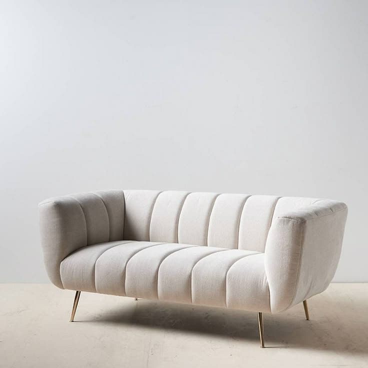 A two-seater sofa with a curved back and arms. The seat and back are upholstered and feature vertical channel tufting. The sofa is supported by thin, tapered metal legs. — 3D model