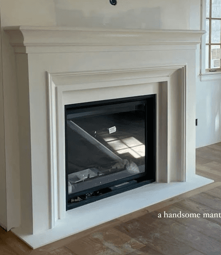 A pristine, white fireplace mantel with a prominent rectangular black insert, presented from an isometric top-down view. The mantel features clean lines with subtle classical-inspired molding along the top and base, and recessed panels on the side pilasters. The overall appearance is sleek and minimalist, suitable for contemporary or transitional interiors. — 3D model