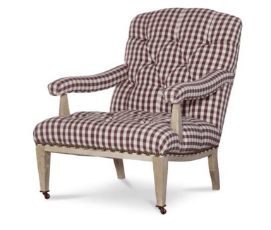 A traditional upholstered armchair featuring a maroon and white gingham check pattern. The backrest and seat are deeply tufted, providing a classic, cushioned appearance. The armrests are also upholstered and gently rolled, supported by exposed light-toned wooden stiles. The chair's frame includes visible wooden legs, with the front legs equipped with brass casters for mobility. Decorative brass nailhead trim outlines the base of the seat where the fabric meets the wooden frame. — 3D model