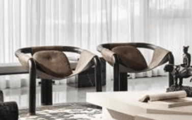 A modern lounge chair featuring a continuous, curved black tubular metal frame that forms the legs, armrests, and back support. A rich brown, possibly suede or durable textile, sling upholstery is draped over the frame, creating a comfortable, relaxed seating surface. A small, padded circular cushion is integrated into the backrest, accented with a single button tuft. — 3D model