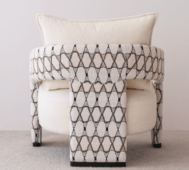 A contemporary upholstered armchair featuring a plush, light-colored bouclé fabric on the seat and back, complemented by patterned armrests and legs with a geometric design in black, white, and a coppery tone. It includes a matching back cushion. — 3D model