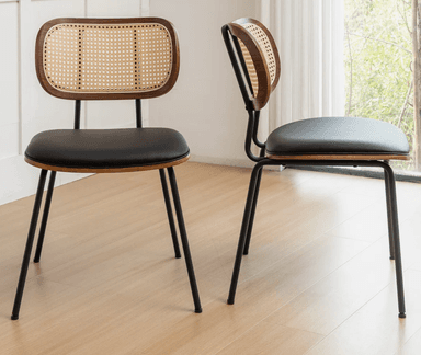 A modern dining chair featuring a bentwood and cane backrest, a black upholstered seat, and a sleek black metal frame. The backrest has a rounded rectangular shape with a dark wood frame encasing a natural woven cane panel. The seat is a padded, square cushion upholstered in a dark, likely faux leather material. The chair is supported by four slender, slightly tapered black metal legs. — 3D model