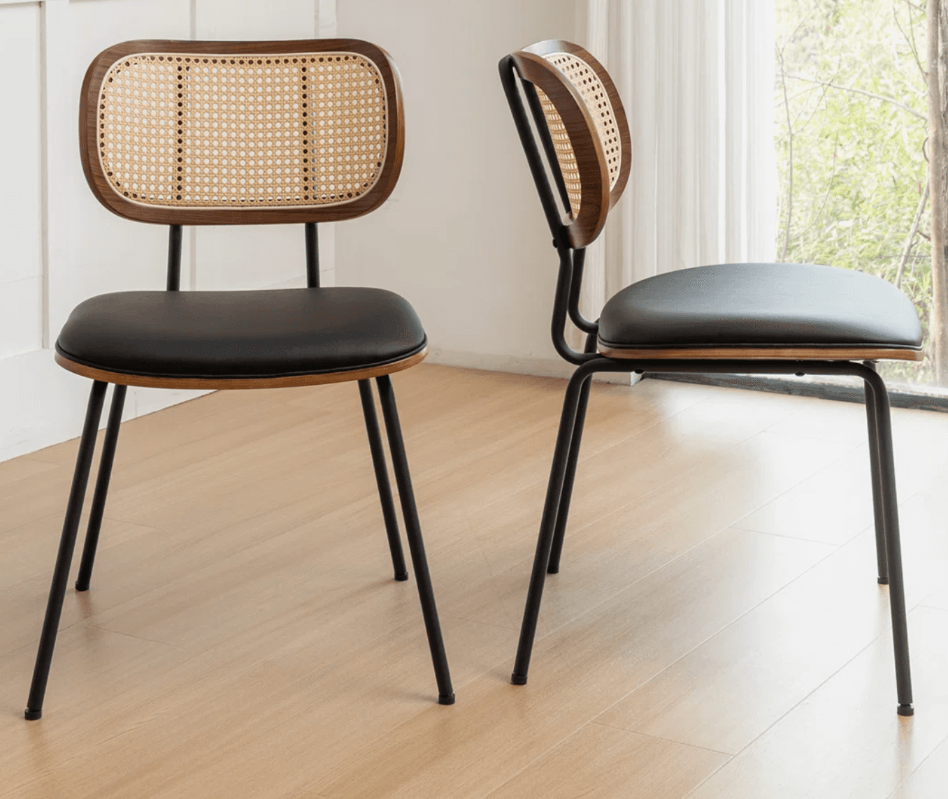 A modern dining chair featuring a bentwood and cane backrest, a black upholstered seat, and a sleek black metal frame. The backrest has a rounded rectangular shape with a dark wood frame encasing a natural woven cane panel. The seat is a padded, square cushion upholstered in a dark, likely faux leather material. The chair is supported by four slender, slightly tapered black metal legs. — 3D model