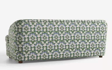 A three-seater sofa with a rounded armrest on the left side. The sofa is upholstered in a fabric with a repeating floral pattern in green, blue, and white. It has a solid base and short, wooden legs. — 3D model