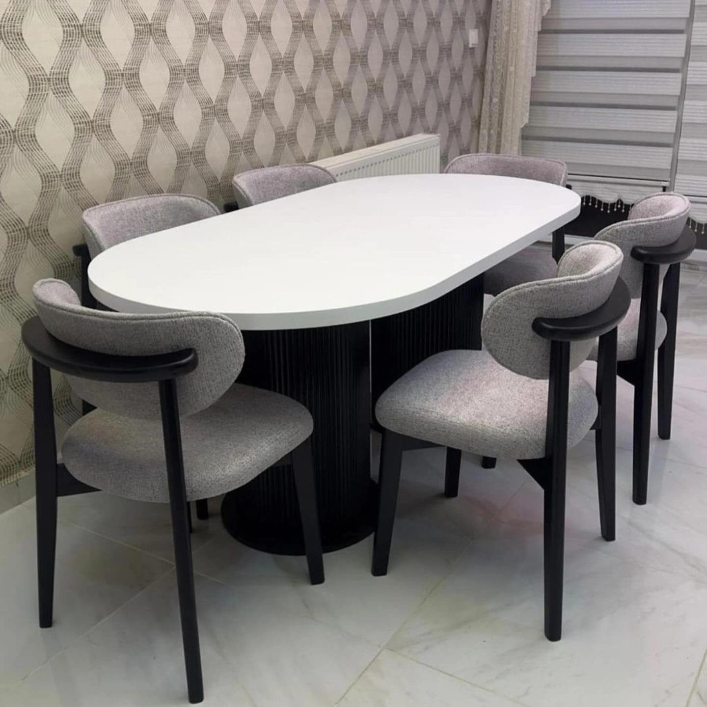 A modern dining set featuring an oval-shaped, white tabletop supported by a fluted cylindrical pedestal base in black. The set includes six upholstered chairs with a light grey textured fabric, featuring a curved backrest and dark wooden legs and armrests. — 3D model