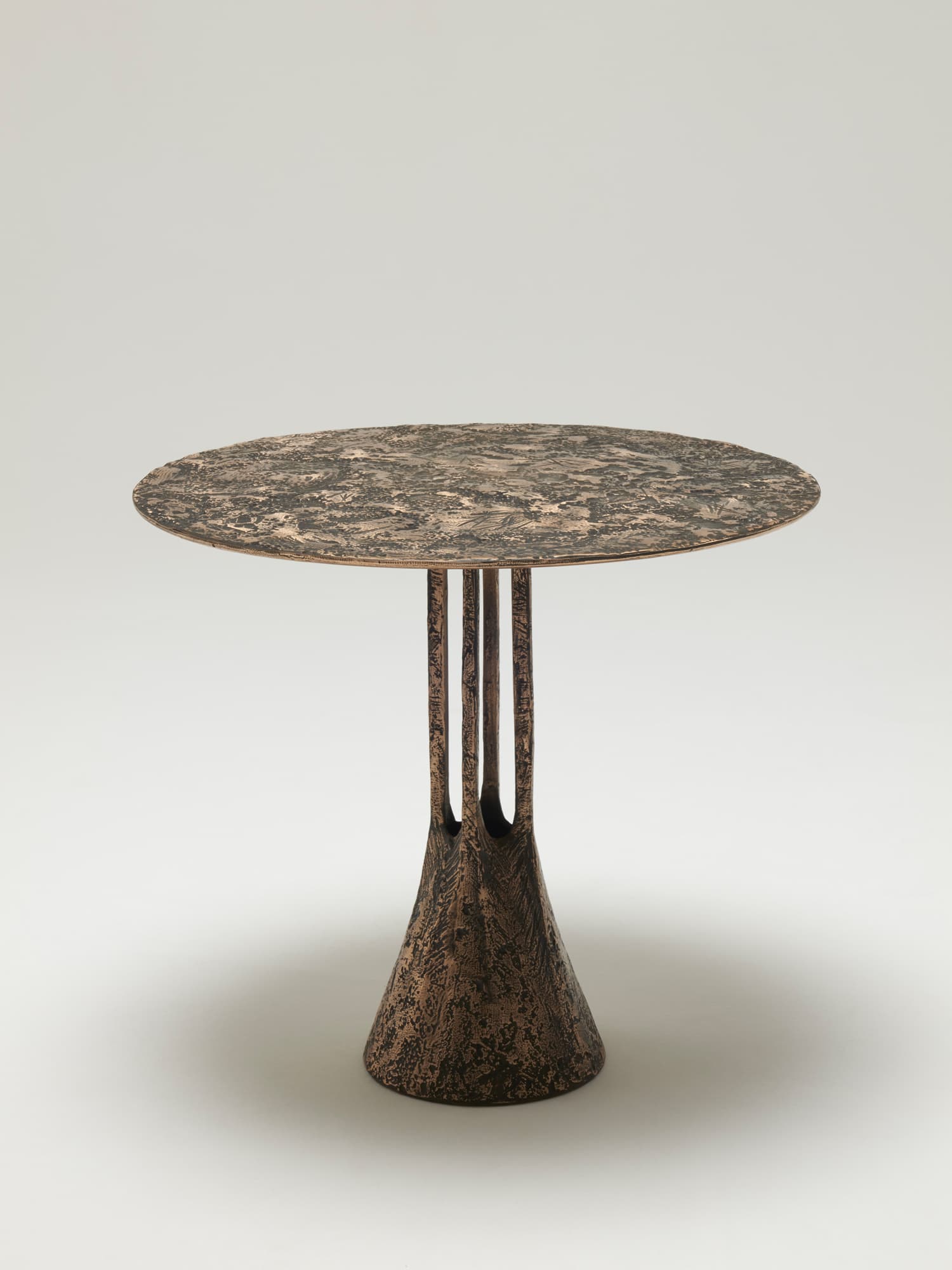 A striking pedestal side table featuring a round top and a conical base, both exhibiting a heavily textured, organic, and distressed bronze-like finish. The base transitions into three vertical, textured supports that connect to the tabletop. The overall aesthetic is raw and tactile, suggesting a handcrafted or brutalist-inspired design. — 3D model