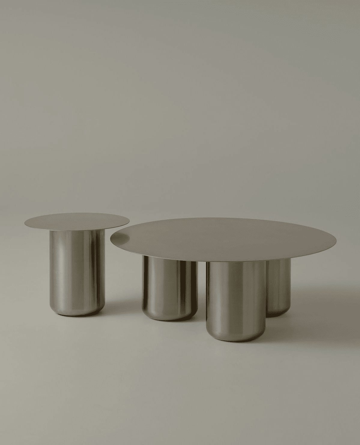 A contemporary coffee table set consisting of a larger, round coffee table and a smaller, side table. Both tables feature a minimalist design with a flat, circular top and a cylindrical pedestal base. The larger table has three cylindrical legs visible, while the smaller table appears to have a single cylindrical leg. The construction suggests a hollow metal form, likely for weight reduction and structural integrity. The overall aesthetic is sleek and modern. — 3D model