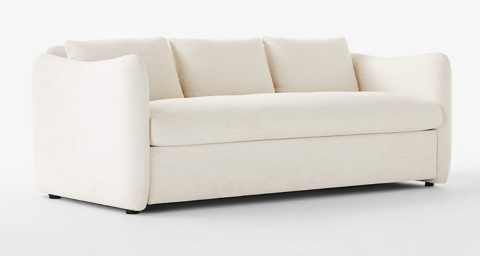 A modern, low-profile sofa with a creamy off-white textured upholstery. It features generously padded seat and back cushions, with three plush throw pillows arranged across the back. The arms are wide and gently curved, blending smoothly into the base. The sofa has a streamlined, contemporary design with dark, short, block feet. — 3D model