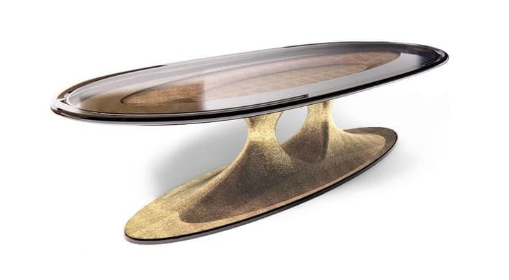 An oval coffee table featuring a smoked glass top with a patterned insert, supported by a sculptural, hourglass-shaped base with a textured, metallic finish. The design exhibits a contemporary and organic aesthetic. — 3D model