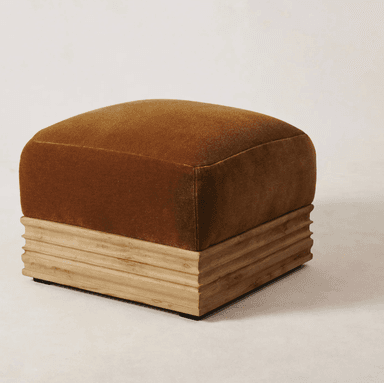 A square-shaped ottoman with a plush, upholstered top and a fluted wooden base. The upholstery is a deep, rich ochre or burnt orange color with a soft texture, possibly velvet. The base is constructed from wood with a natural finish, featuring horizontal, carved grooves that give it a ribbed appearance. The overall design blends soft, tactile materials with a structured, textured base. — 3D model