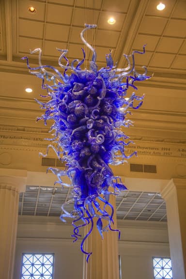 A large, elaborate chandelier constructed from numerous individual pieces of hand-blown art glass. The fixture features a voluminous, cascading form composed primarily of deep cobalt blue glass elements, including swirling tendrils, bulbous forms, and some leaf-like shapes, creating an organic and sculptural aesthetic. — 3D model