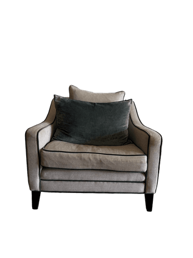 A contemporary upholstered armchair featuring a light, textured fabric and dark contrasting piping. It has a deep seat, padded armrests, and comes with a matching back pillow and a dark green velvet throw pillow. The chair is supported by dark, low-profile tapered legs. — 3D model