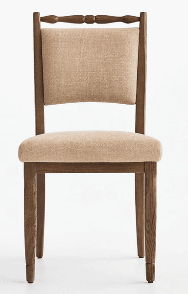 A traditional wooden dining chair featuring an upholstered seat and backrest, and a distinctive turned spindle top rail. The frame is made of dark brown wood, possibly oak, with visible grain. The seat and back are padded and covered in a light beige, textured fabric. The legs are tapered, with the back legs subtly splayed. — 3D model