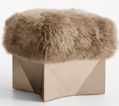 A modern ottoman featuring a textured, fur-like upholstered top and a geometric base. The top is rounded and appears to be made of a long-pile material, while the base is angular with faceted sides. — 3D model