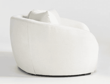 A close-up view of a cream-colored sofa, focusing on the armrest and seat cushions. The upholstery appears to be a textured boucle or similar woven fabric. The armrest has a rounded, curved profile, and the seat cushions are plush with visible stitching. The base of the sofa, where it meets the floor, is partially visible and appears to be a dark wood. — 3D model