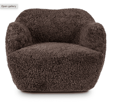 A dark brown armchair with a plush, textured upholstery resembling sheepskin or fleece. The chair features a rounded, organic silhouette with integrated armrests that flow seamlessly into the back and seat. The base is wide and solid, with no visible legs, giving it a grounded appearance. The overall design suggests a modern and comfortable aesthetic. — 3D model