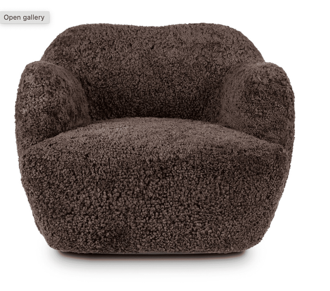 A dark brown armchair with a plush, textured upholstery resembling sheepskin or fleece. The chair features a rounded, organic silhouette with integrated armrests that flow seamlessly into the back and seat. The base is wide and solid, with no visible legs, giving it a grounded appearance. The overall design suggests a modern and comfortable aesthetic. — 3D model