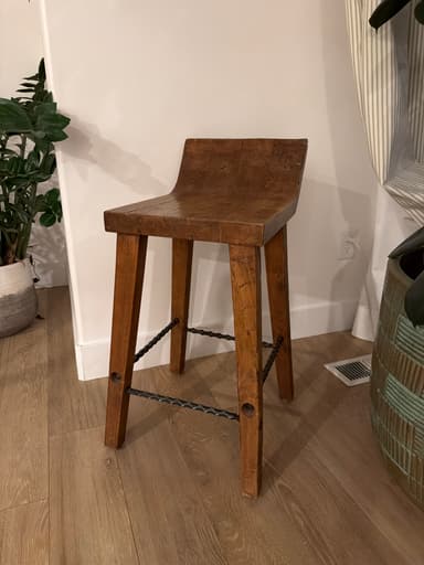 A rustic wooden stool with a contoured seat and four angled legs connected by a black metal support brace. — 3D model