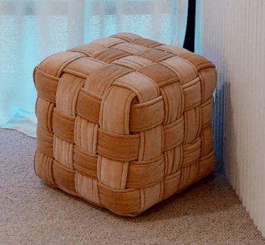 A cube-shaped ottoman featuring a distinctive woven exterior made from padded strips of beige velvet fabric. The interwoven pattern creates a plush, textured surface. — 3D model