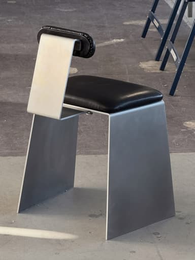 An armless chair with a minimalist design, featuring a bent metal frame in a matte silver finish and a black faux leather upholstered seat and a small backrest. — 3D model