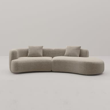 A large, modular, curved sofa with a textured, boucle-like upholstery. The sofa features rounded edges and appears to be composed of at least two connected sections, forming a sweeping arc. It includes two square throw pillows that match the sofa's upholstery. The design is contemporary with a soft, inviting aesthetic. — 3D model