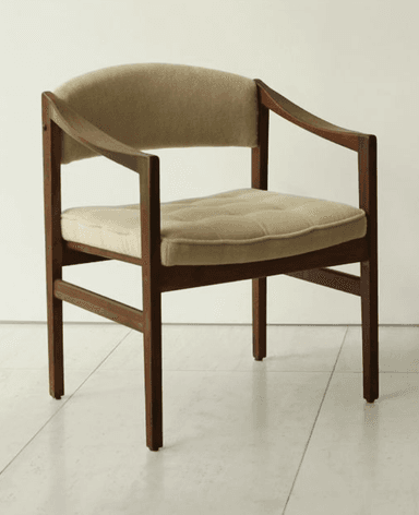 A mid-century modern armchair featuring a dark wood frame and light beige fabric upholstery. The chair has a clean, rectilinear wooden frame with subtly curved armrests. Both the seat and back are padded, with the seat cushion exhibiting button tufting, suggesting a comfortable yet structured design. The wooden legs are straight, and the overall aesthetic is minimalist and functional. — 3D model