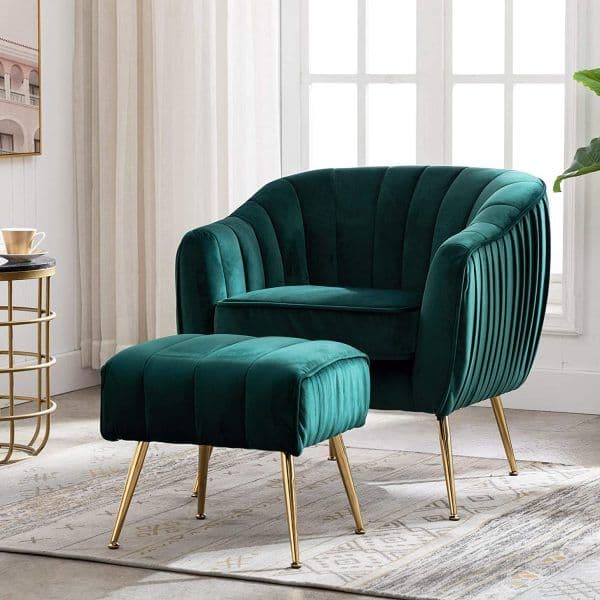 An emerald green velvet armchair with a distinctive channel-tufted design on its curved back and sides, paired with a matching rectangular ottoman. Both pieces feature tapered gold-finished metal legs, contributing to a glamorous aesthetic. The armchair has a deep, plush seat cushion, and the ottoman is also upholstered in channel-tufted velvet. — 3D model