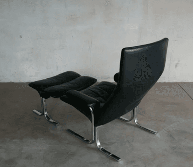 A black leather armchair with a matching ottoman. The chair features a high back and a curved, cantilevered chrome base. The ottoman also has a curved chrome base and is upholstered in matching black leather with a segmented cushion design. — 3D model