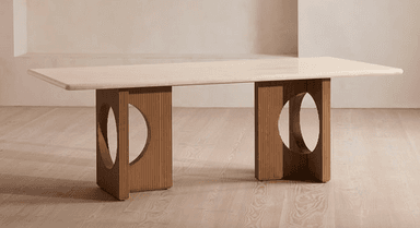 A long, rectangular dining table featuring a light-colored travertine top with rounded corners. The top is supported by two substantial, medium-toned wooden pedestal bases. Each base is characterized by vertical fluting or reeding and a large, semicircular cutout on its inner side, creating a sculptural and architectural aesthetic. — 3D model