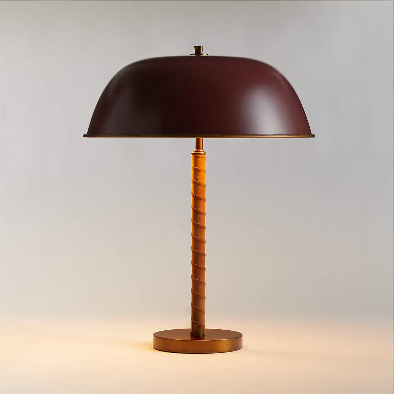 A contemporary table lamp featuring a deep maroon domed metal shade, brass accents, and a cylindrical stem wrapped in tan leather, resting on a round brass base. — 3D model