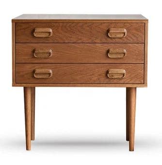 A compact, light-toned wooden chest of drawers featuring three stacked drawers and supported by four round, tapered legs. The design incorporates integrated, scoop-style drawer pulls, suggesting a Mid-Century Modern or Scandinavian aesthetic. The wood grain is visible and consistent across all surfaces, indicating solid wood or high-quality veneer construction. — 3D model