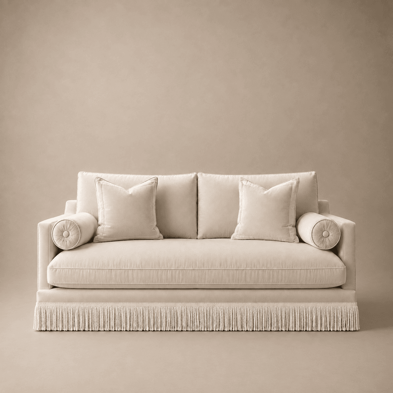 A contemporary upholstered sofa featuring a solid, boxy frame and a distinctive fringed skirt base. The sofa is finished in a plush, light beige velvet-like fabric, complemented by two loose seat cushions, two loose back cushions, and two round bolster cushions on the arms. The design blends modern lines with a classic decorative detail. — 3D model