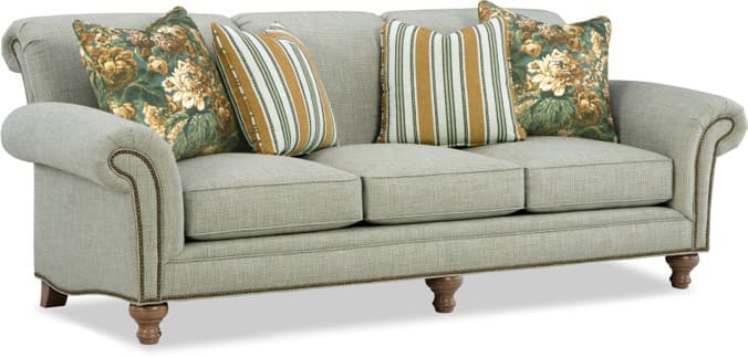 A traditional style three-seater sofa featuring light-colored, textured fabric upholstery, rolled arms, and decorative nailhead trim along the front and base. It has three loose seat cushions, three attached back cushions, and is supported by four turned wooden legs. The sofa comes with a mix of floral and striped accent pillows. — 3D model
