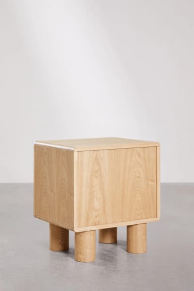 A contemporary nightstand with a cuboid main body and four cylindrical legs. The top and side panels have gently rounded edges. The grain of the wood is clearly visible, suggesting a natural wood construction. — 3D model