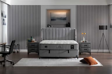 A modern upholstered bed frame with a tufted headboard and a mattress. The bed frame is upholstered in a textured gray fabric and features two integrated drawers at the foot of the bed. The mattress is white with a patterned quilted top and a gray border. The headboard has vertical channel tufting. The bed is supported by slender black legs. — 3D model