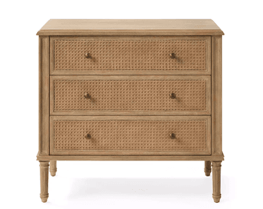 A light wood chest of drawers featuring three drawers with woven rattan fronts, supported by four elegantly fluted, turned legs. It has a classic rectangular silhouette with a slightly overhanging top and brass knob hardware. — 3D model