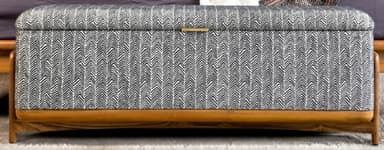 An upholstered storage bench featuring a grey and white herringbone pattern fabric and an exposed light-toned wooden frame. The top functions as a lift-lid with a small brass pull handle. — 3D model