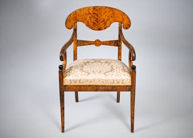 An antique armchair featuring a distinctive curved and carved backrest, likely made from curly maple or birch wood with a warm, amber finish. The chair has an upholstered seat covered in a cream-colored damask fabric with a patterned motif. The back legs are straight and square-tapered, and the back structure includes carved elements that function as armrest supports. The overall design suggests a formal, historical aesthetic. — 3D model