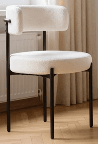 A modern accent chair with a black metal frame and a plush, textured cream-colored upholstery. The seat is round and thickly padded, and the backrest is a gently curved, low profile with a cylindrical armrest integrated into one side. The legs are slim and angled. — 3D model
